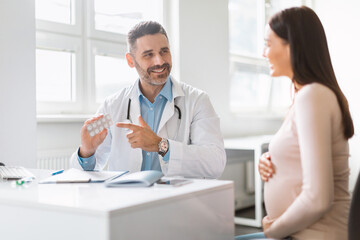 Healthy habits for pregnancy. Happy male therapist prescribing vitamins for young pregnant woman