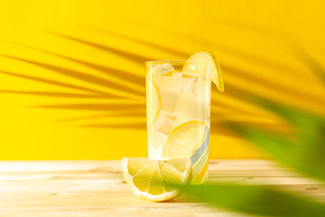 Front view of a lemonade glass with ice cubes and palm leaf shadow over a wooden table