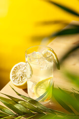 Vertical top angle view of lemonade with ice cubes on a wooden table and palm leaf