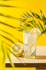 Vertical frontal view of a lemonade glass with ice cubes on a wooden table and palm leaf
