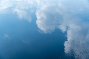Fototapeta premium Blue sky mirror reflection and beautiful clouds in river. Ripple of heaven on surface water of white cumulus clouds. Abstract calm nature background. Pattern and wallpaper of amazing cloudscape.