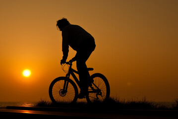 Fototapeta na wymiar silhouet of a young adult riding a bike at sunset