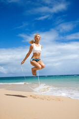 Caucasian young adult woman jumping rope on beach.