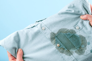 Men hands showing a dirty stain shirt and visual evaluation of stain on clothes on a blue...