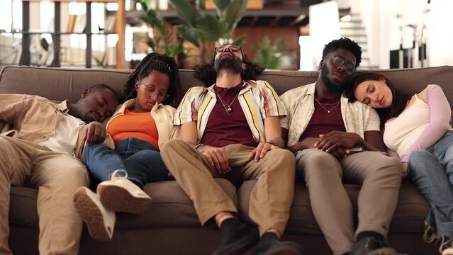 Party multiracial friends, drunk and hungover sleeping on a sofa in the living room after the celebration. Drinking, hangover and alcohol, coworking workers at break sleeping on the sofa
