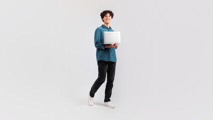 Cheerful Young Man Holding Computer Standing Over Yellow Studio Background