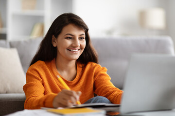 Positive young indian woman student attending webinar, using laptop
