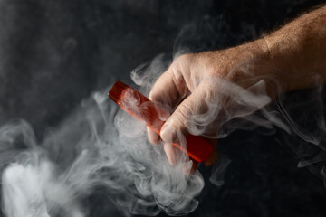 disposable electronic cigarette in a man's hand on a dark background with smoke around. The concept...