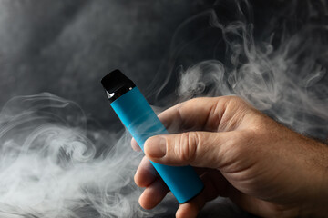 disposable electronic cigarette in a man's hand on a dark background with smoke around. The concept...