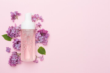 Foaming facial cleanser and with flowers on color background, top view