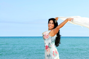 Fototapeta na wymiar Portrait of beautiful smiling brunette girl at beach with arms outstretched