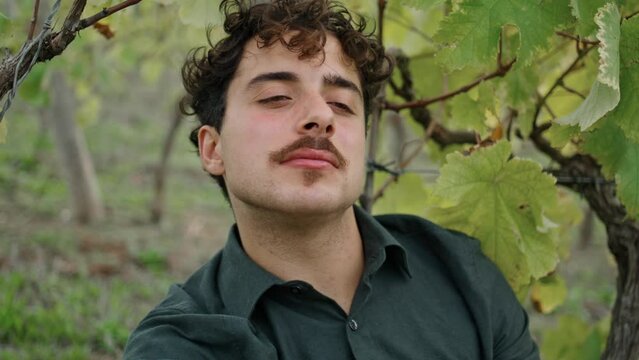 Portrait young man winegrower sitting under vine eating grapes. Worker relaxing.