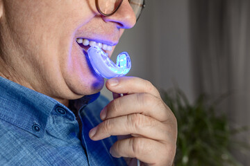 an aged man is engaged in teeth whitening at home using a mouth guard with an LED lamp, a snow-white smile, dental care, dentistry