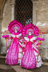 Fototapeta na wymiar Gorgeous masquerade ladies in pink dresses at Piazza San Marco, Venice