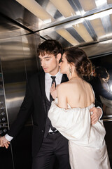 good looking groom in formal wear pushing button while hugging brunette and young bride in wedding dress and standing together in elevator of modern hotel © LIGHTFIELD STUDIOS