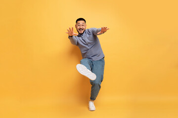 Fototapeta na wymiar Cheerful young asian man having fun on yellow studio background