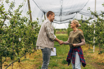 A man and a woman shaking hand in an orchard.