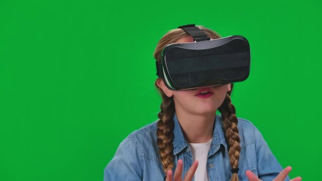 Absorbed teen girl enjoying augmented reality gaming in VR headset on green screen. Close-up concentrated happy relaxed Caucasian teenager playing video game in virtual reality