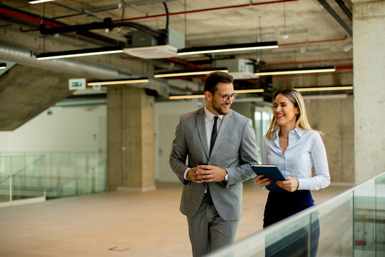 Young coworkers walking and talking along corridor in modern office