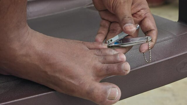 Close-up of a man cutting the toenails with a nail clipper on a chair