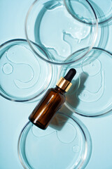 Cosmetic beauty concept with bottle serum, drops and petri dish on blue background