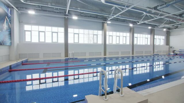 New large swimming pool in brightly lit hall of sports complex. Modern athletic school equipment ready for opening. Recreation center