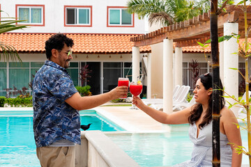 A young latin couple toasting drinks and enjoying by the poolside on a sunny day