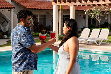 A young latin couple toasting drinks and enjoying by the poolside on a sunny day