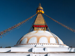 Buddhist stupa with prayers flags and a yellow lotus painted in the dome and bright blue sky. Nepal.