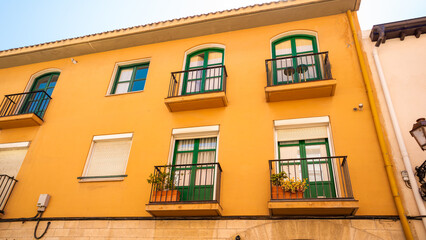 Yellow building balconies with green doors and flower pots