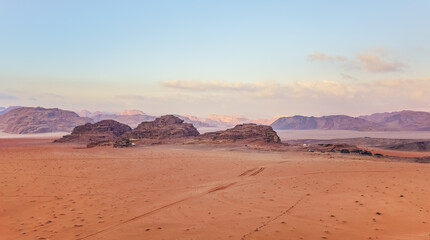Fototapeta na wymiar Orange red sand desert, rocky formations and mountains background, blue sky above, camp tents visible at distance - typical scenery in Wadi Rum, Jordan