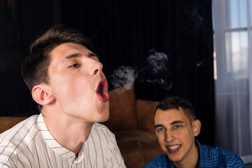 Young man demonstrating his vape smoking skills to his friends, trying to make smoke rings.