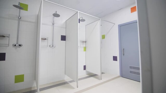 Public shower cabins with chrome heads in gym bathroom. Place for body wash in modern sports club and swimming pool. School washroom equipment