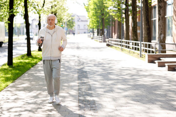 Mature Man Jogger Is Running Straight In The Street Wearing Headphones Listening To Music. Sport And Healthy Lifestyle Concept