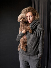 happy girl with a dog in a photo studio on gray. chocolate Poodle and curly woman
