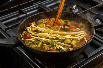 Frying pan with chopped stewed vegetables in sauce and spices with udon.