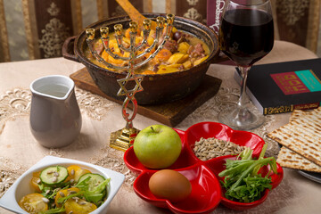 A set table for the Passover Seder with traditional matzah, wine, maror and a hot cholent for the meal.