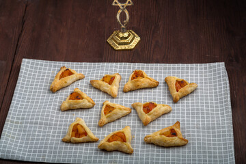 Sweet gomentashi cookies for the holiday of Purim on a blackboard are laid out on a gray napkin next to the menorah.