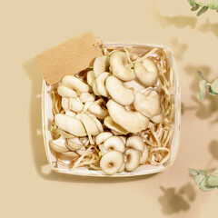 Edible mushrooms. Close-up organic oyster mushrooms in a wooden box with empty label on beige background with leaves. Natural products and healthy vegan or vegetarian food. Flat lay