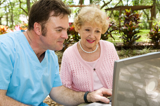 Senior lady receiving help on the computer from a nursing home orderly.