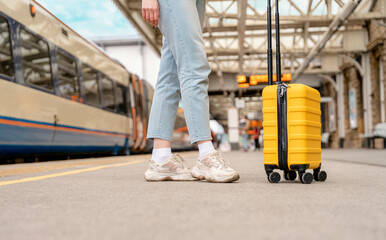 Traveler with a yellow suitcase waiting for a train at the train station on the platform. Travel concept.