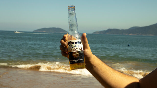 M&atilde;o masculina segurando uma garrafa de cerveja corona em uma praia de Ilhabela. Foto feita em S&atilde;o Paulo, Brasil em 10 Nov 2023.