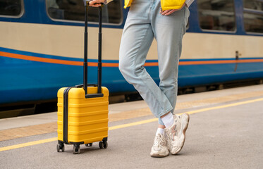 Traveler with a yellow suitcase waiting for a train at the train station on the platform. Travel...