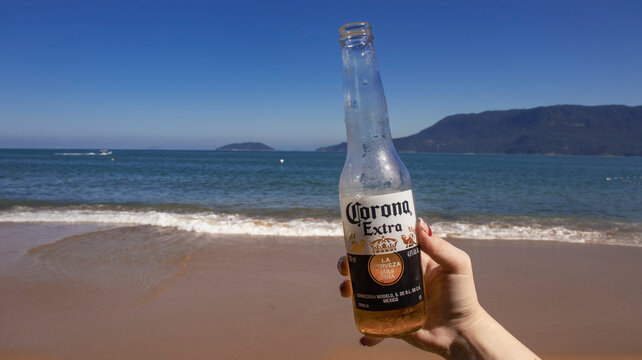 person on the beach holding a corona beer bottle. Photo made in Ilhabela, SP, Brazil in 10 July 2023