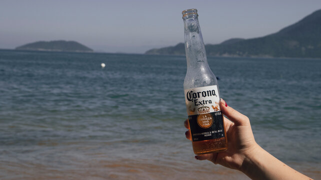 person on the beach holding a corona beer bottle. Photo made in Ilhabela, SP, Brazil in 10 July 2023