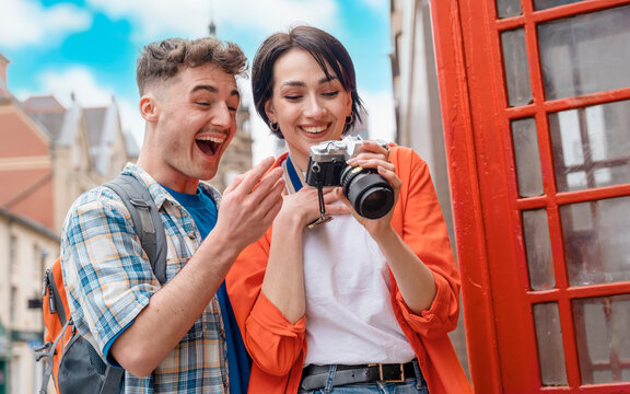 two friend, couple using a camera,   taking selfie against a red phonebox, watching photos on camera, having a fun  in the city of England.Travel Lifestyle concept