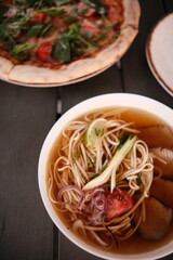pho broth, Vietnamese soup in a deep plate with meat, wooden Chinese sticks and two quail eggs on a dark background