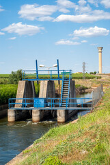 Compuertas de un canal de riego, con estación elevadora de agua al fondo, usada para que el agua fluya por el canal. Imagen vertical.