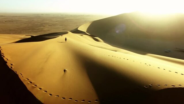 Travel, desert and silhouette of man at sunset with drone for destination, freedom or summer trip. Footprints, adventure and journey with guy on horizon of sand dunes on trip of Dubai vacation