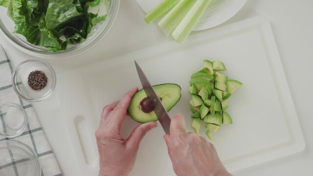 Woman removing the avocado pit. Green salad with celery, lettuce, and avocado recipe. Ingredients close-up on white background